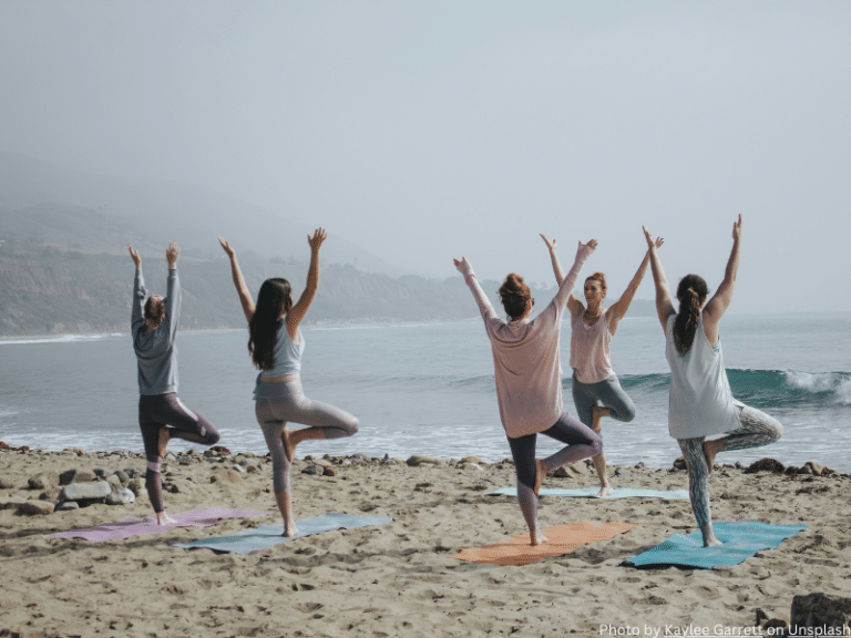 Group of women practicing yoga on the beach, representing physical and mental self-care